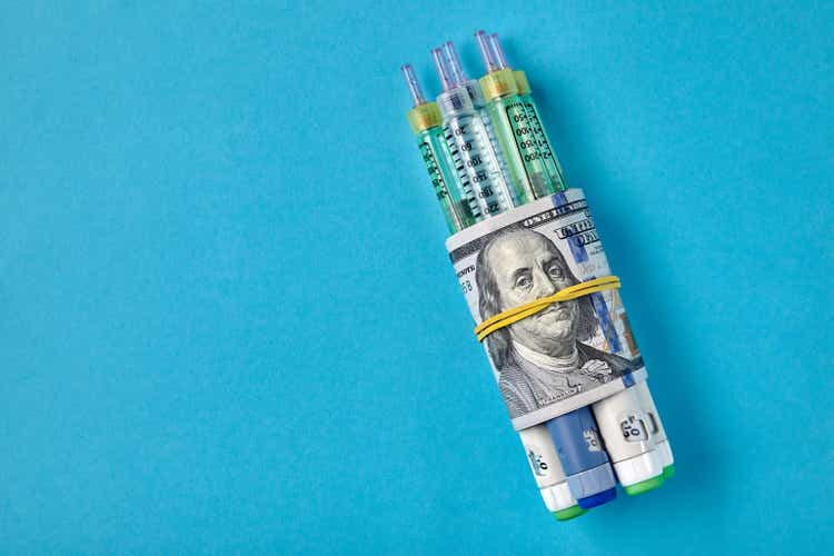 Insulin syringe pens wrapped in dollar bills on a blue background